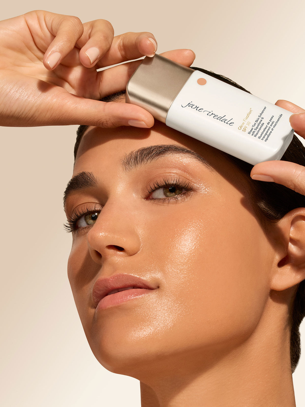 Person hält die Flasche des jane iredale Glow Fixation SPF 30 über der Stirn. Das Gesicht zeigt einen gleichmäßigen, leicht strahlenden Teint.
