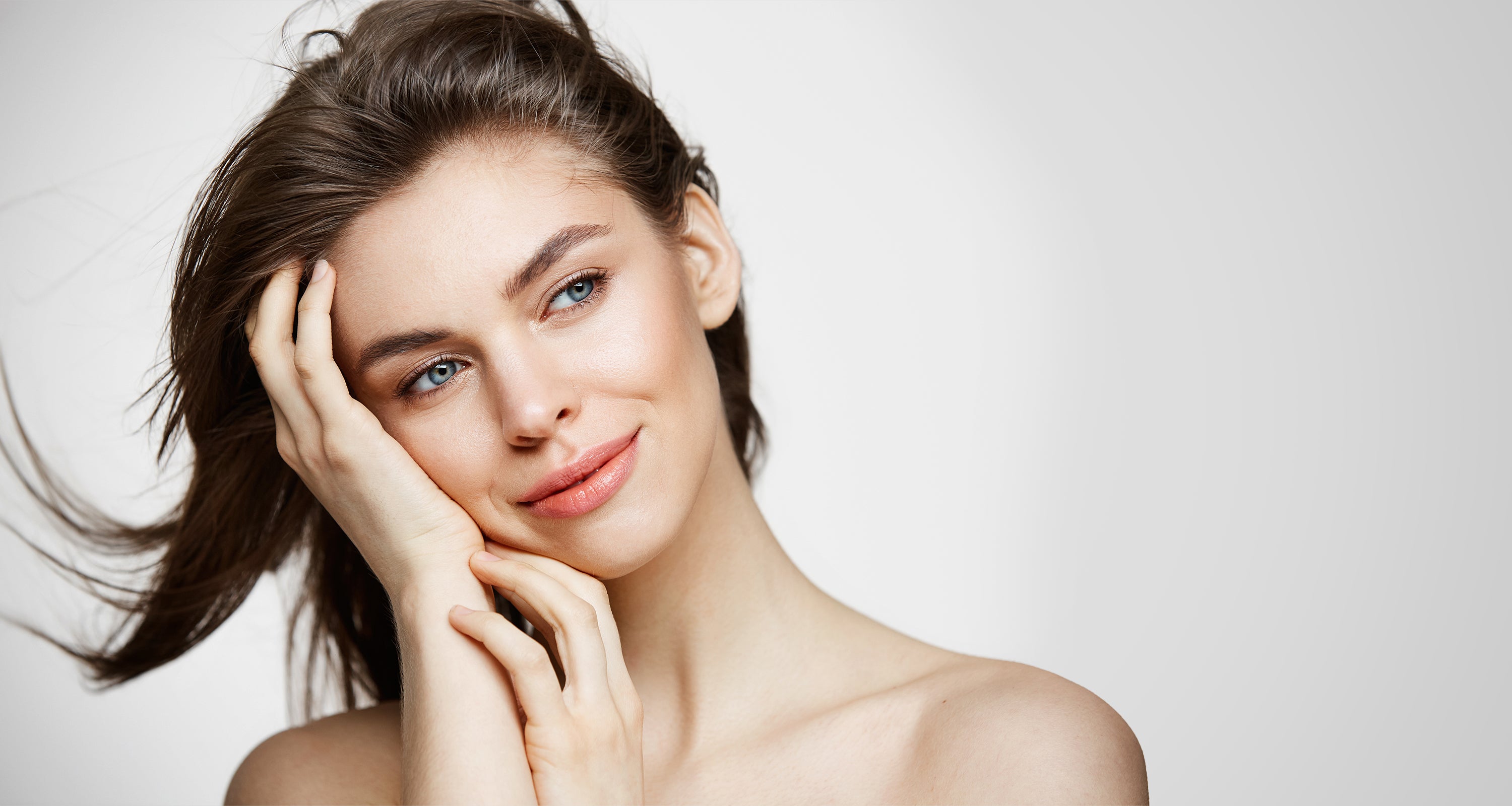 Eine junge Frau mit brunettem Haar und blauen Augen hält den Kopf zur Seite, aufgestützt auf der rechten Hand und lächelt an der Kamera vorbei