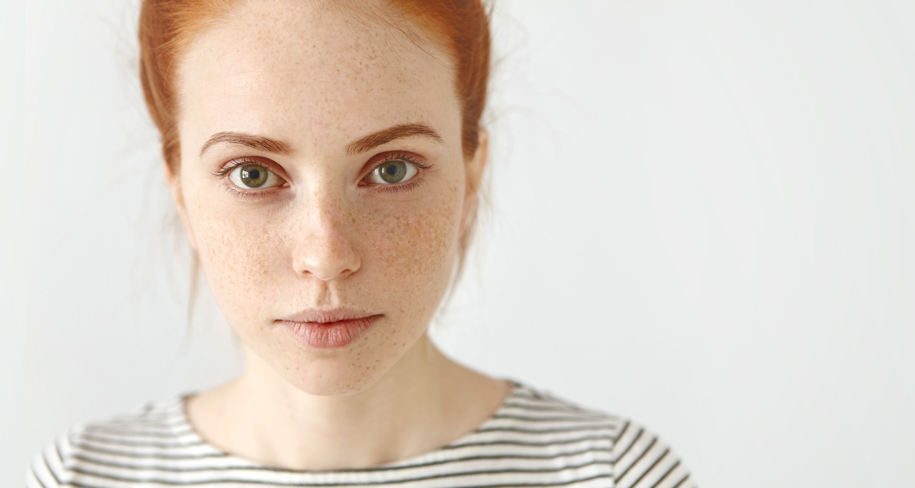 Eine junge Frau mit grünen Augen, Sommersprossen und roten Haaren sowie einem gestreiften T-Shirt schaut in die Kamera