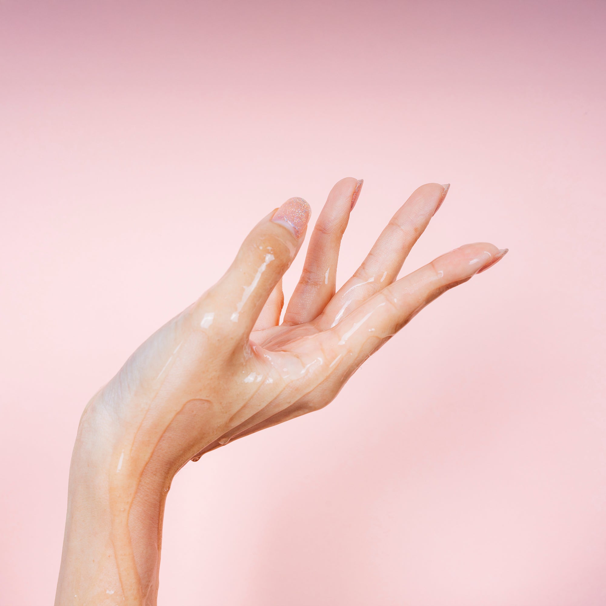 Nahaufnahme einer Hand mit glänzender, feuchter Haut vor einem sanft rosa Hintergrund.