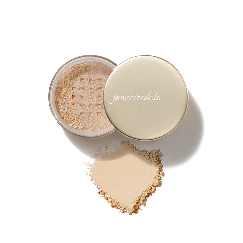 Geöffnete Dose des jane iredale Amazing Base Mineral Powder mit losem Mineralpuder. Vor der Dose ist ein herzförmiger Puderauftrag auf weißem Hintergrund zu sehen.