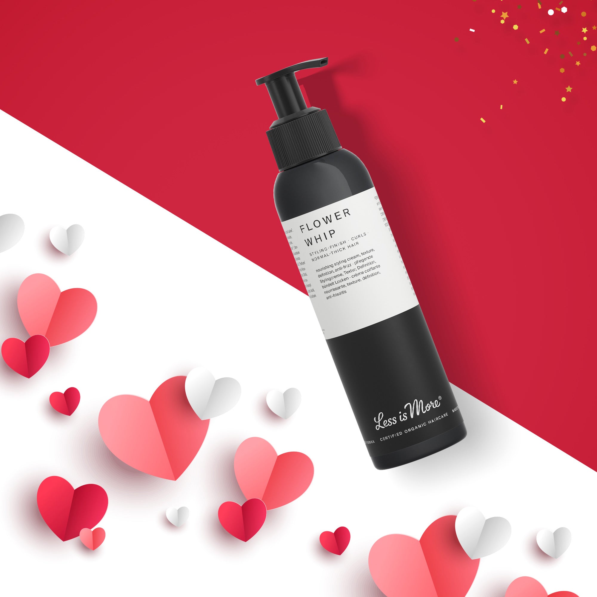 Schwarze Pumpflasche mit weißem Etikett der Marke „Less is More“, Produktname „Flower Whip“. Die Flasche liegt schräg auf einem rot-weißen Hintergrund. Rundherum befinden sich rote, rosafarbene und weiße Papierherzen sowie etwas goldener Konfettiglanz.