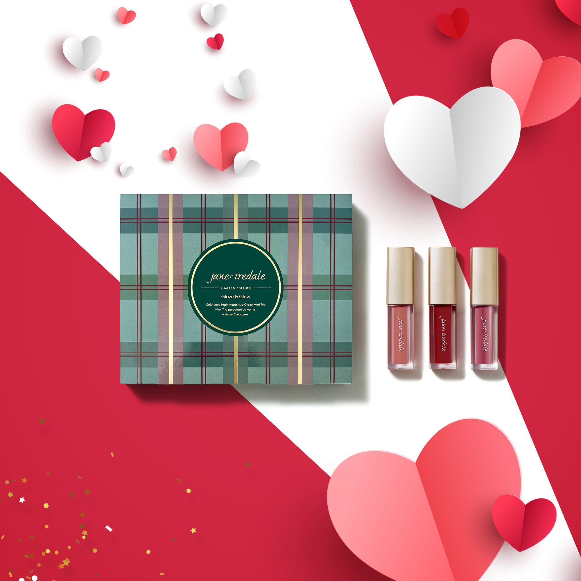 Geschenkbox im karierten Grün-Violett-Design mit rundem Etikett „Jane Iredale – Glaze & Glow“. Rechts daneben stehen drei Lippenprodukte in transparenten Behältern mit goldenem Deckel. Das Set liegt auf einem rot-weißen Hintergrund, dekoriert mit roten, rosafarbenen und weißen Papierherzen sowie goldenem Konfetti.
