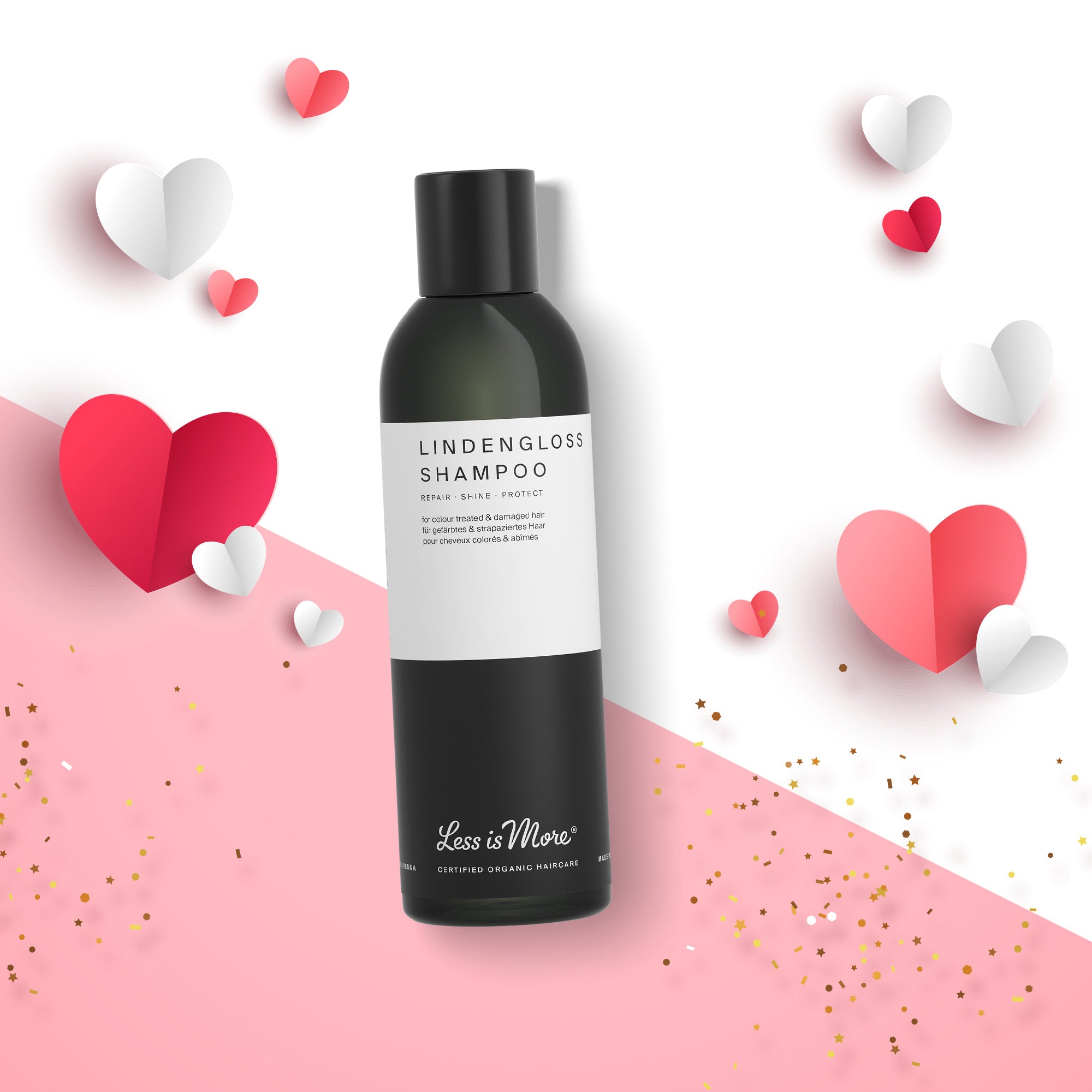 Schwarze Flasche mit weißem Etikett der Marke „Less is More“, Produktname „Lindengloss Shampoo“. Die Flasche liegt schräg auf einem weißen und rosa Hintergrund. Mehrere Papierherzen in Rosa, Rot und Weiß sowie goldener Konfetti sind dekorativ darum verteilt.