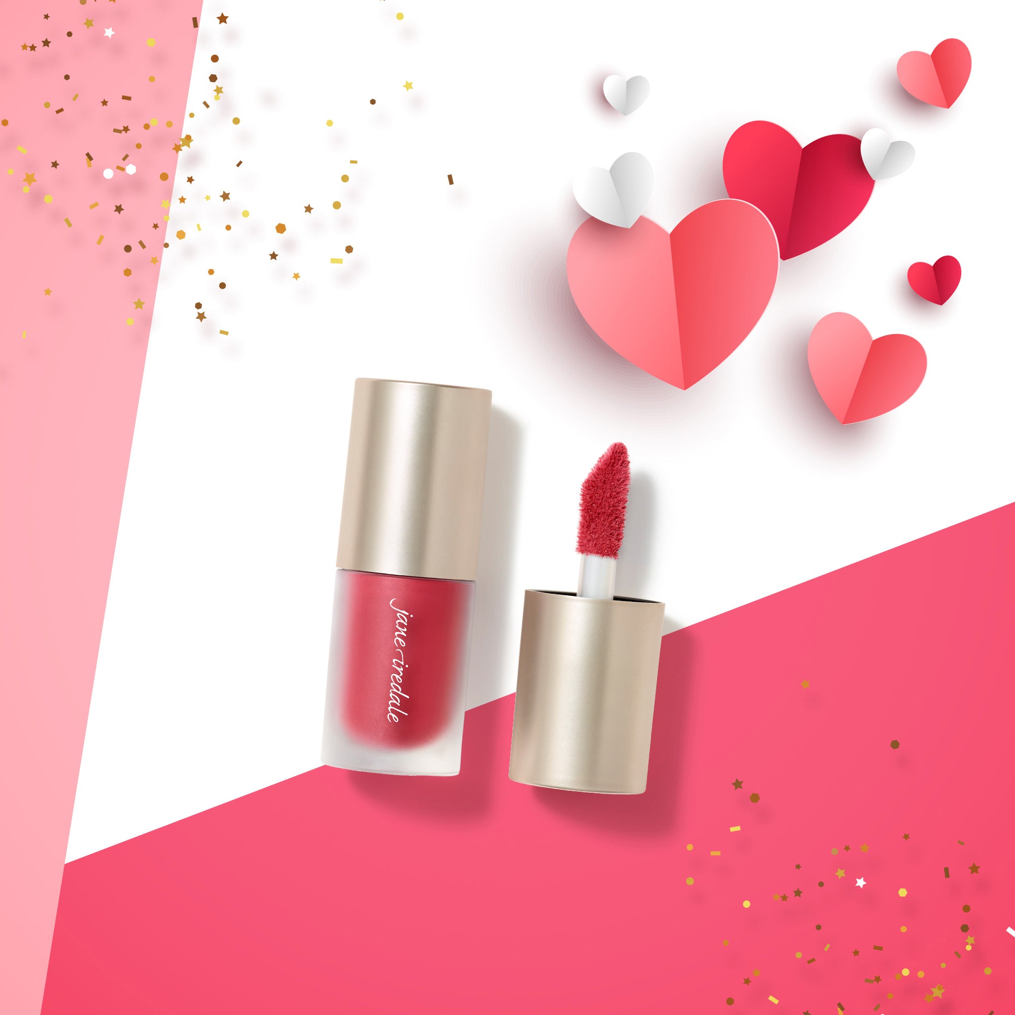 Offener Behälter mit flüssigem Rouge in Rosarot, daneben der abgeschraubte Deckel mit Applikator. Das Produkt liegt auf einem weiß-rosa Hintergrund, umgeben von dekorativen roten, rosafarbenen und weißen Papierherzen sowie goldenem Konfetti.