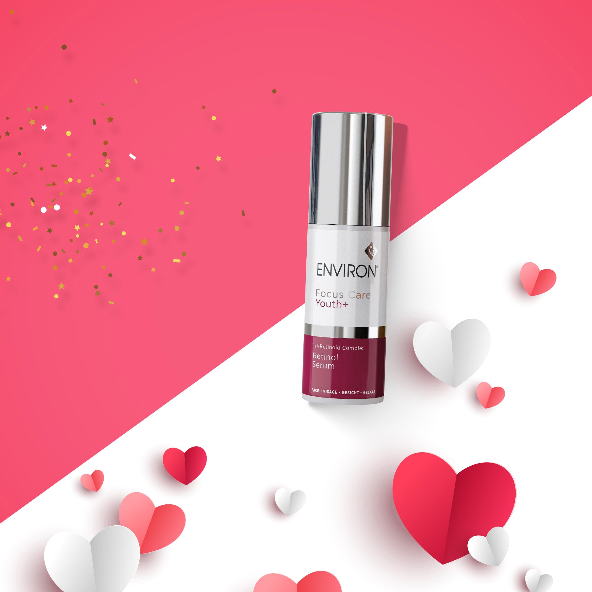 Zylindrischer Pumpspender „Environ Focus Care Youth+ – Retinol Serum“ in Weiß und Dunkelrot mit silbernem Deckel. Das Produkt steht auf einem diagonal geteilten weiß-rosa Hintergrund, dekoriert mit Papierherzen in verschiedenen Rot- und Rosatönen sowie goldenem Konfetti.