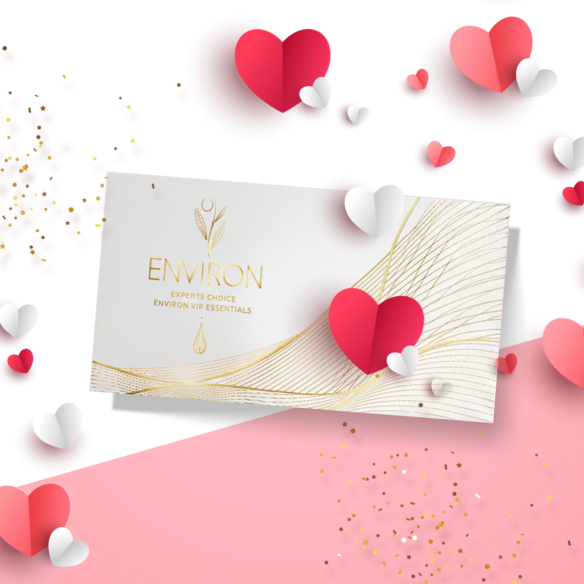 Weiße Geschenkbox mit goldenem Logo und goldenen grafischen Linien, Aufschrift „Environ – Experts Choice – Environ VIP Essentials“. Die Box liegt auf einem rosa-weißen Hintergrund und ist von dekorativen Papierherzen in Rot, Rosa und Weiß sowie goldenen Konfettipartikeln umgeben.