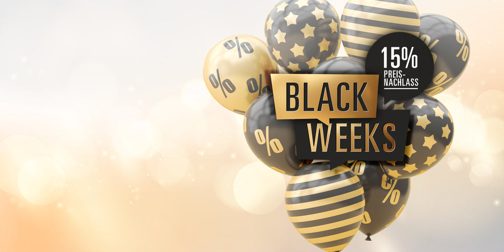 Schwarze und goldene Luftballons mit Prozentzeichen, Sternen und Streifen, darauf der Schriftzug ‚BLACK WEEKS‘ und ein rundes Label mit ‚15 % Preisnachlass‘ vor einem hellen, festlich leuchtenden Hintergrund.