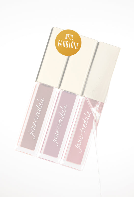 Drei Lipglosse der Marke jane iredale mit goldenen Kappen nebeneinander angeordnet vor weißem Hintergrund. Mittig befindet sich ein goldfarbender Kreis mit der Aufschrift „NEUE FARBTÖNE“.