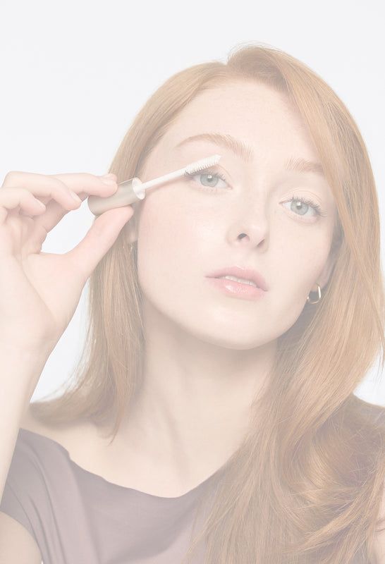 Rothaarige Frau trägt mit einem Applikator einen Lash Conditioner von jane iredale auf ihre Wimpern auf.