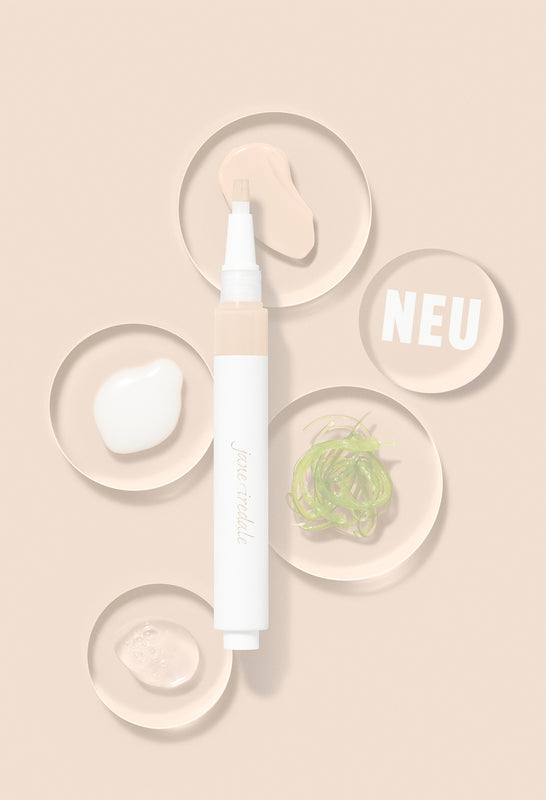 Concealer-Stift der Marke Jane Iredale auf hellbraunem Hintergrund, umgeben von fünf kleinen runden Schälchen. Die Schälchen zeigen verschiedene Texturen und Inhaltsstoffe: weiße Creme, durchsichtiges Gel, grüne Algen und beigefarbene Kosmetikpaste. Ein Schälchen enthält den weißen Schriftzug 'NEU'.