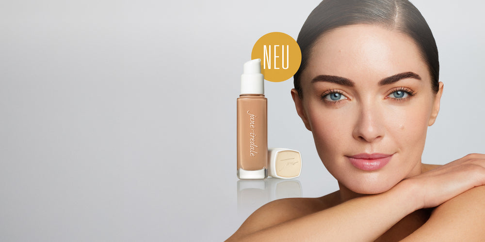 Ein Model schaut freundlich aber neutral in die Kamera, daneben eine Glasflasche der jane iredale Flüssigfoundation Skintuition und das Wort NEU in einem Kreis